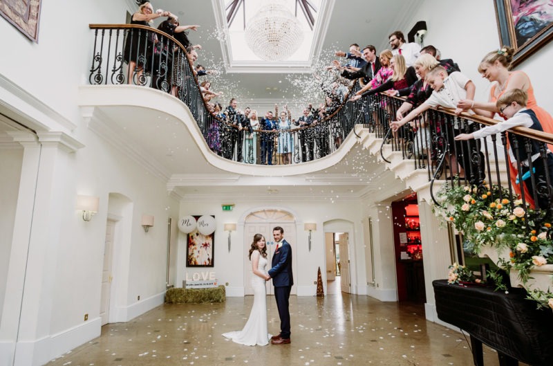 The happy couple hand in hand as confetti falls down above them