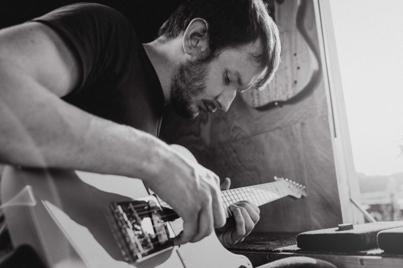 Black and white close up of Ed playing guitar with sun flare coming through window