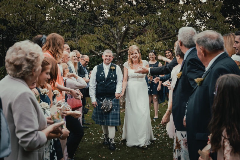 Newly weds walking towards camera laughing under a shower of confetti
