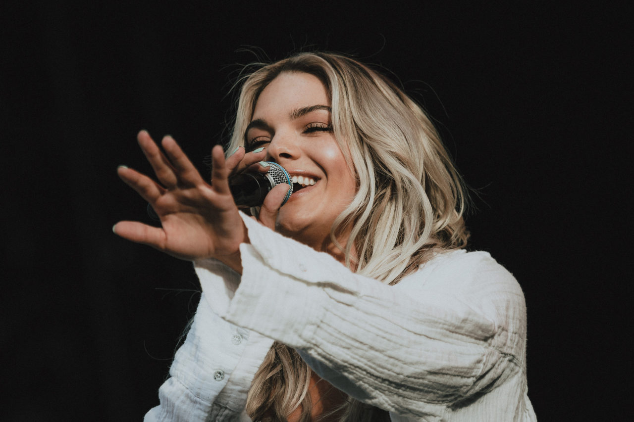Female popstar Louisa Johnson smiling with microphone andhand reaching out to the audience