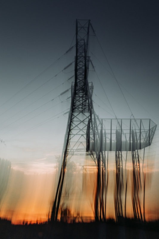 Pylon stood in a field against a twilight sun in gradient of colour