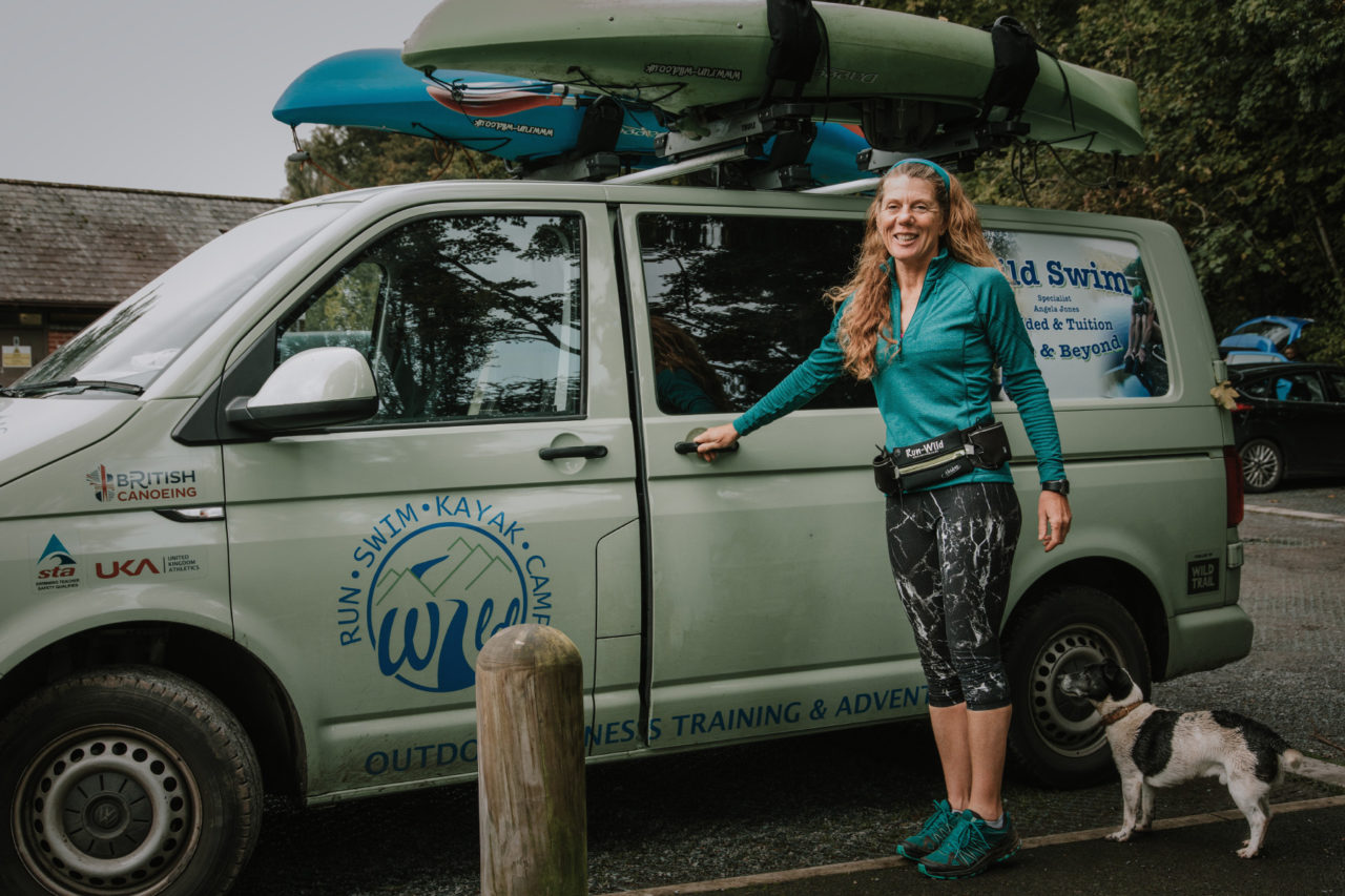 Lady stood in front of VW Transporter van with kayaks on roof and dog in foreground