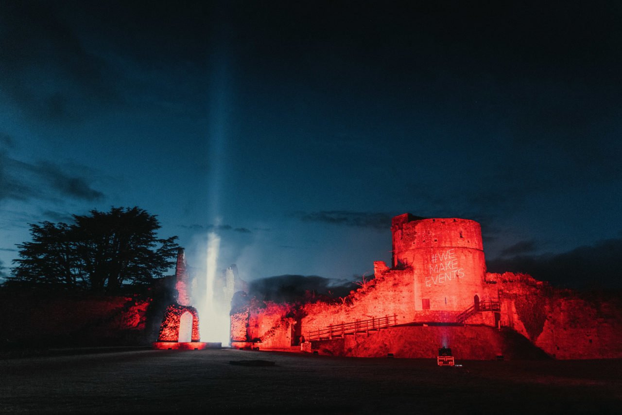 Castle illuminated in red with a spot light shining up into the night sky
