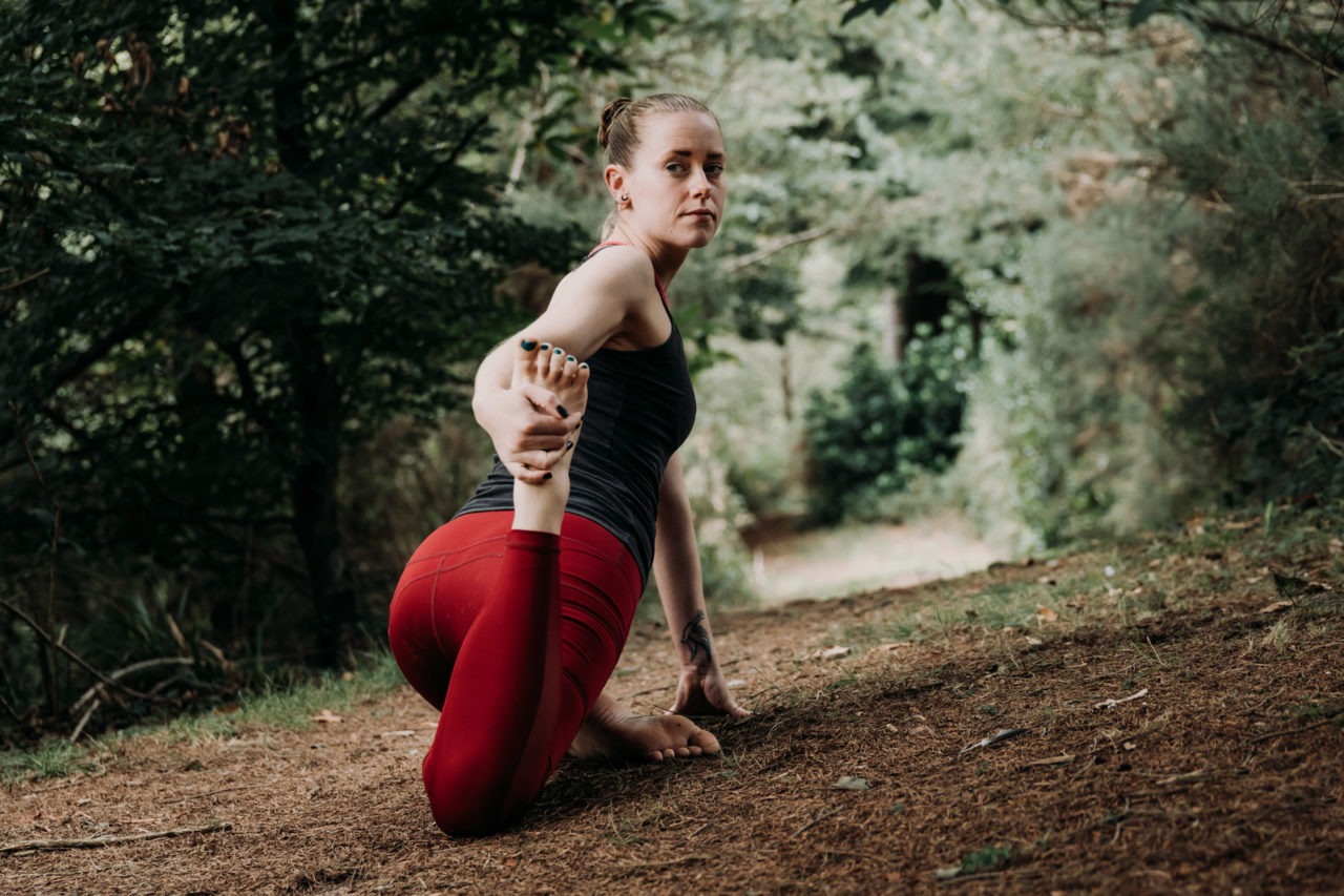 Girl in forest knelt down reaching back to hold leg