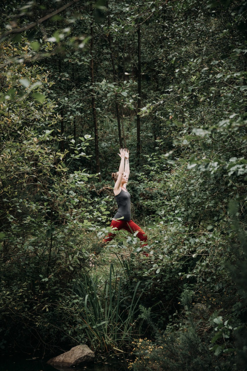 View from across lake of girl in forest with arms stretched up high