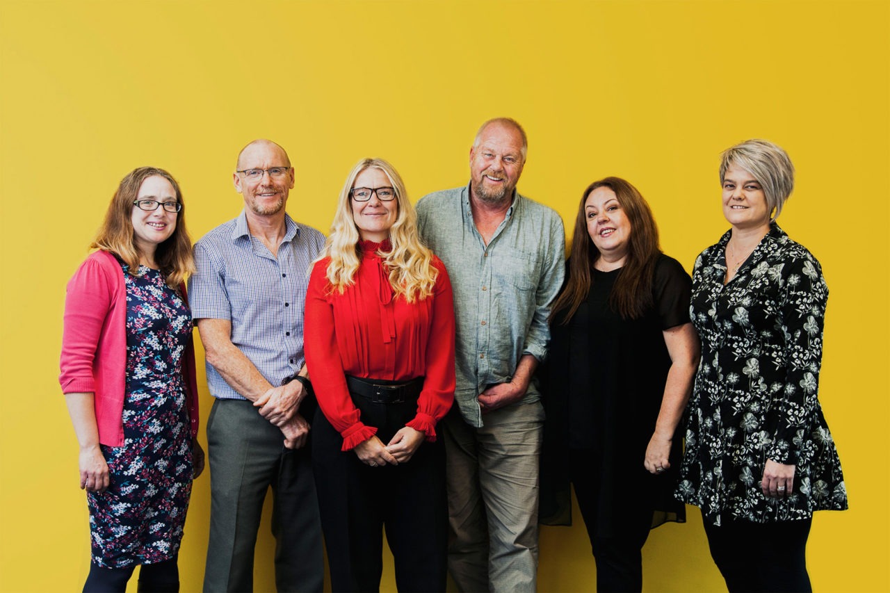 Friendly looking team stood smiling against a yellow backdrop