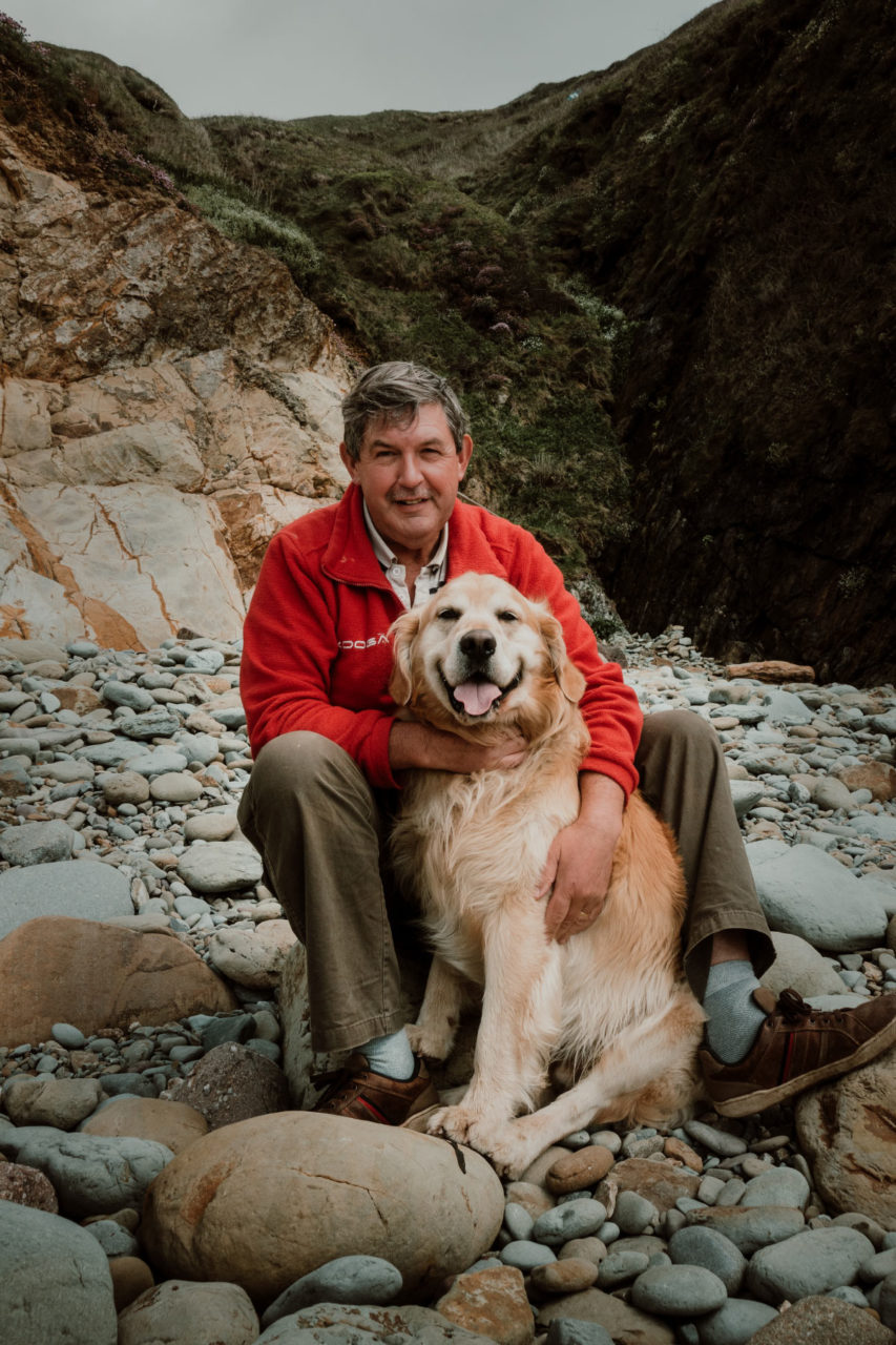 Man sat on rocky beach hugging his happy labrador