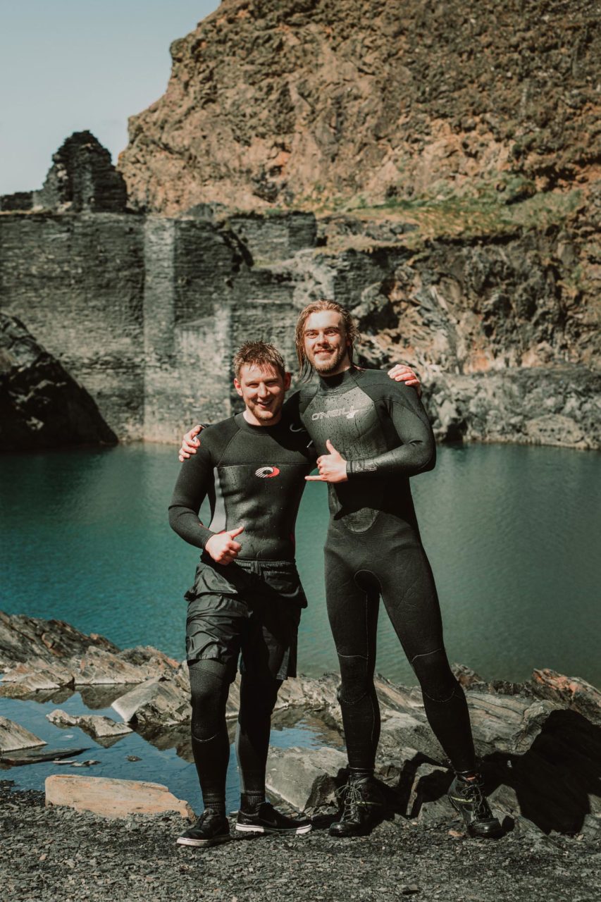 Two cliff divers staring triumphantly at the camera with blue lagoon behind