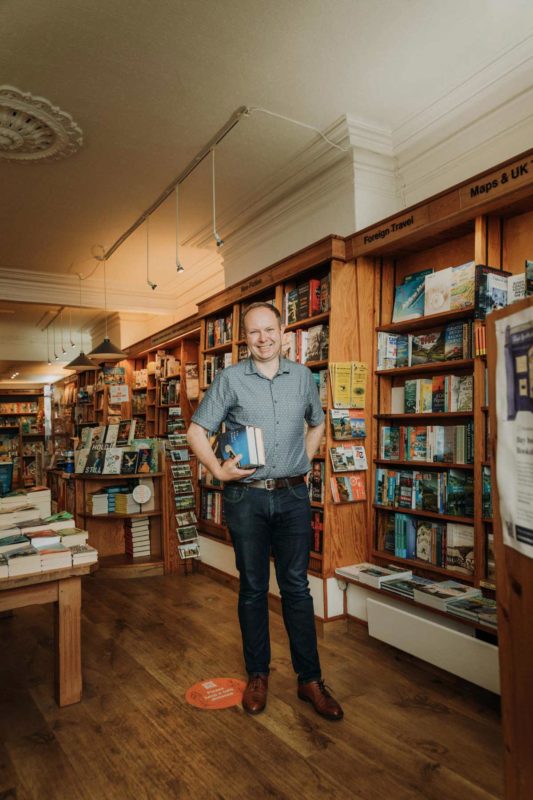 Bookshop owner stood smiling with books under his arm