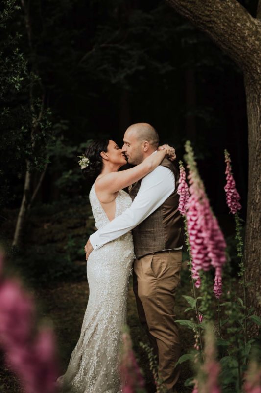 Newly weds stood kissing in fairytale-esque forest