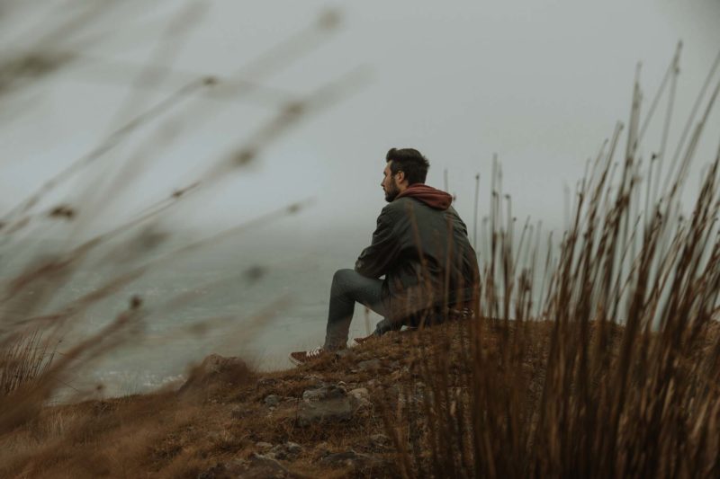 Back of man sitting on a moutain viewed through the undergrowth