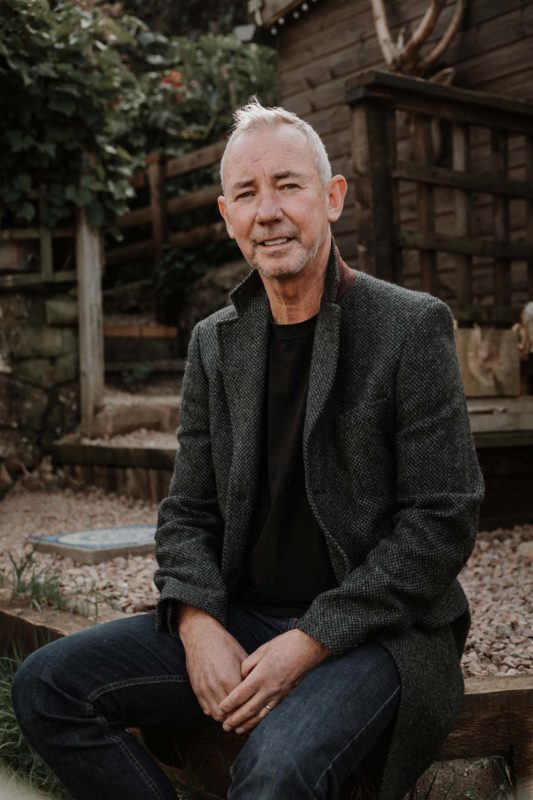 Relaxed man sat on decking gazing sincerely into the camera