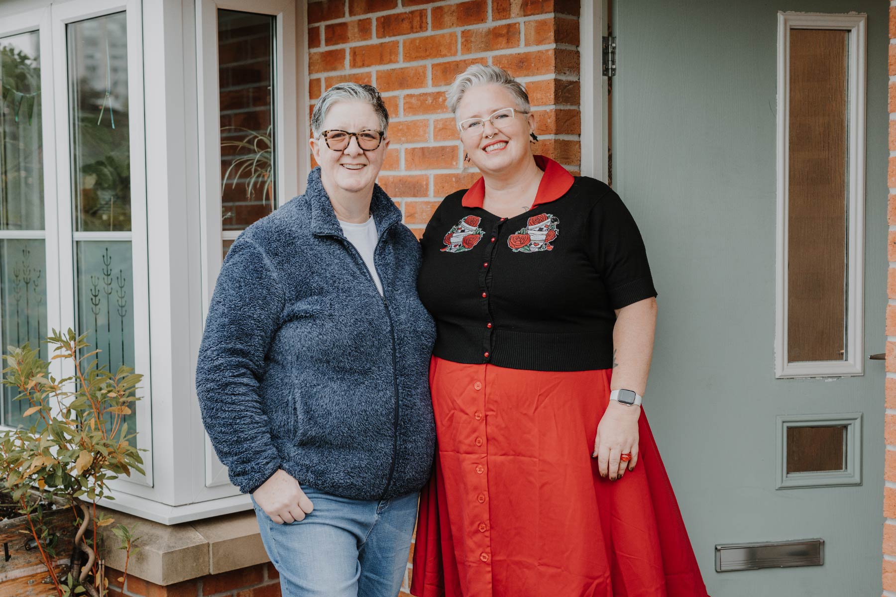 Female couple stood smiling in front of olive green door