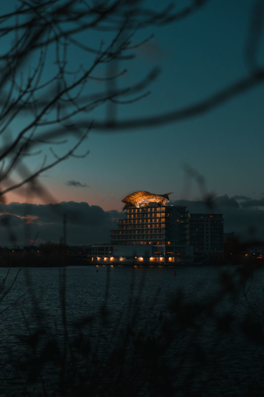 Shot of a hotel with lights on from across a bay as the sun sets