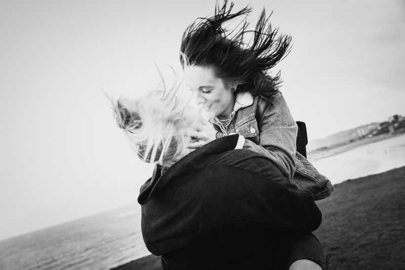 Newly engaged woman sharing a kiss in the wind on top of a cliff
