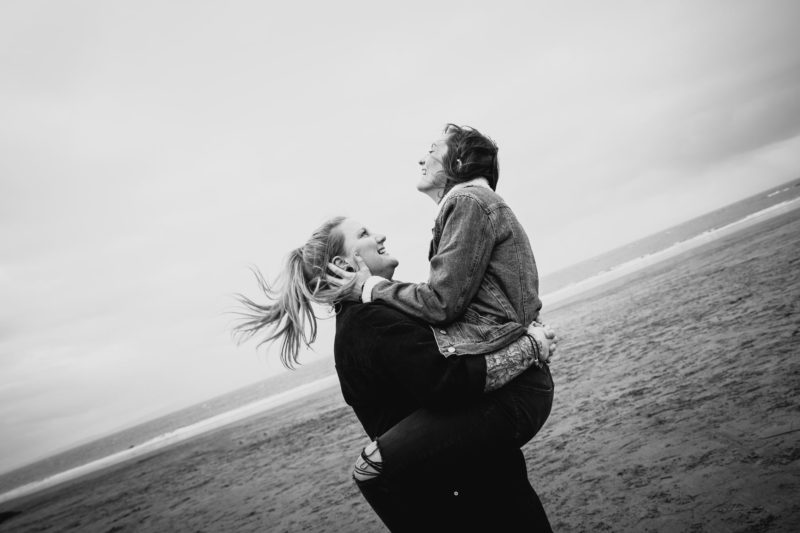 Girl happily lifting her fiancé into air in black and white