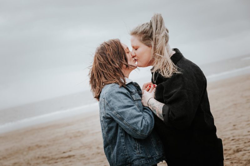 Two woman sharing a kiss, holding hands on a beach