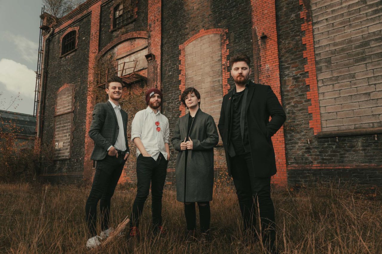 Smartly dressed band stood in front of an old derelict red brick factory