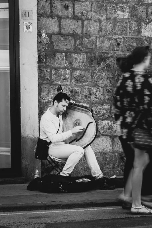 Street performer playing a stringed instrument in Rome while people walk past