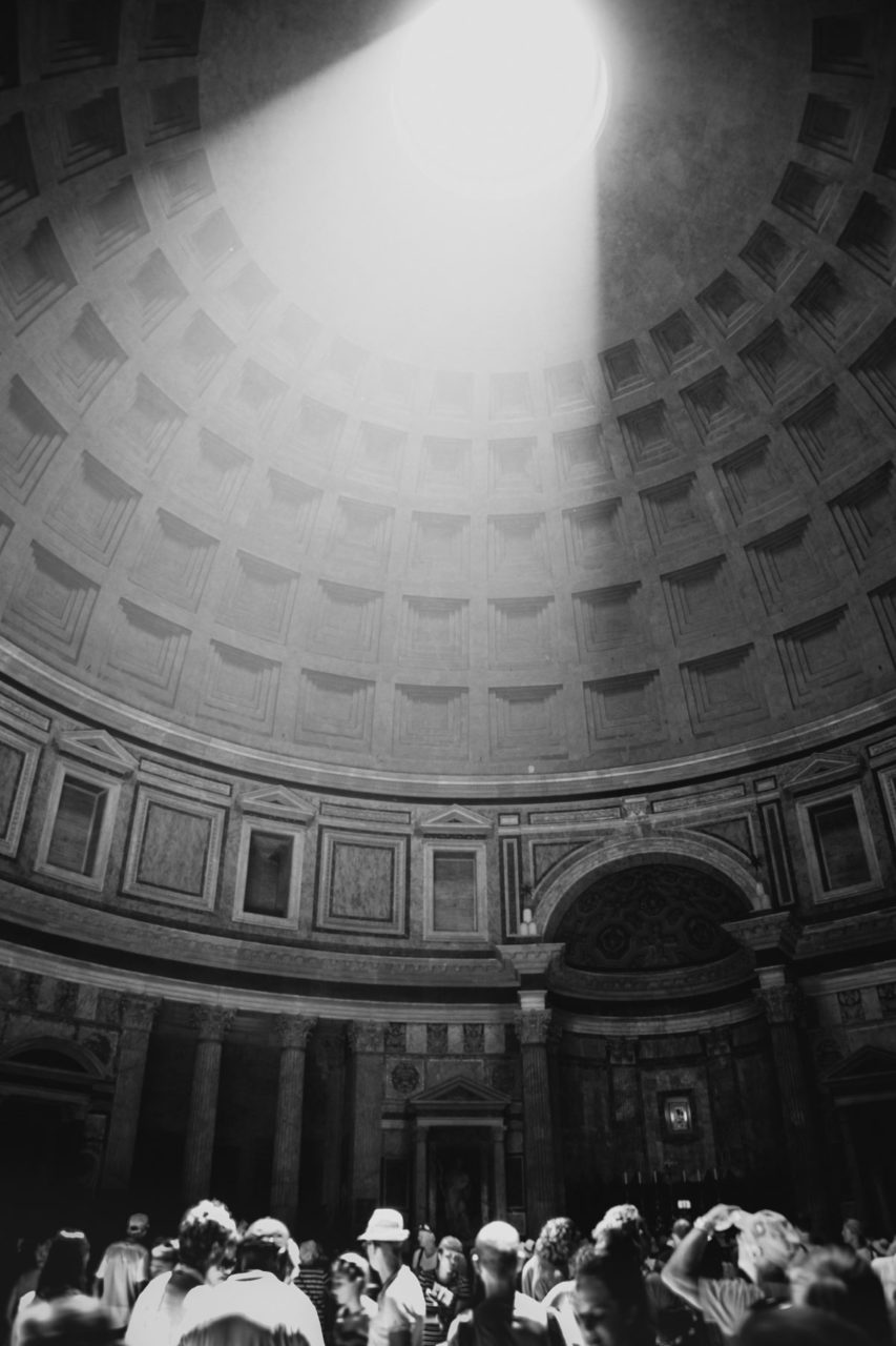 Black and white shot of light rays shining through the ceiling of ancient Roman building