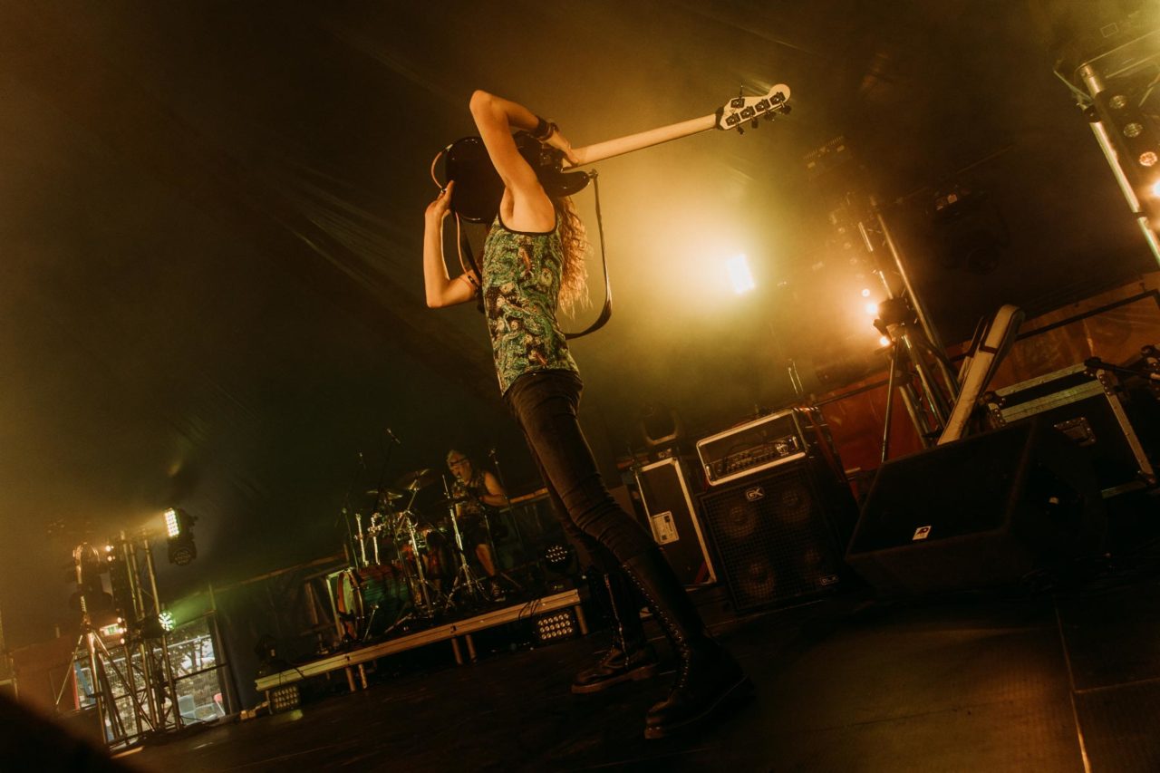 Rock bassist lifting guitar up into the air while playing with teeth