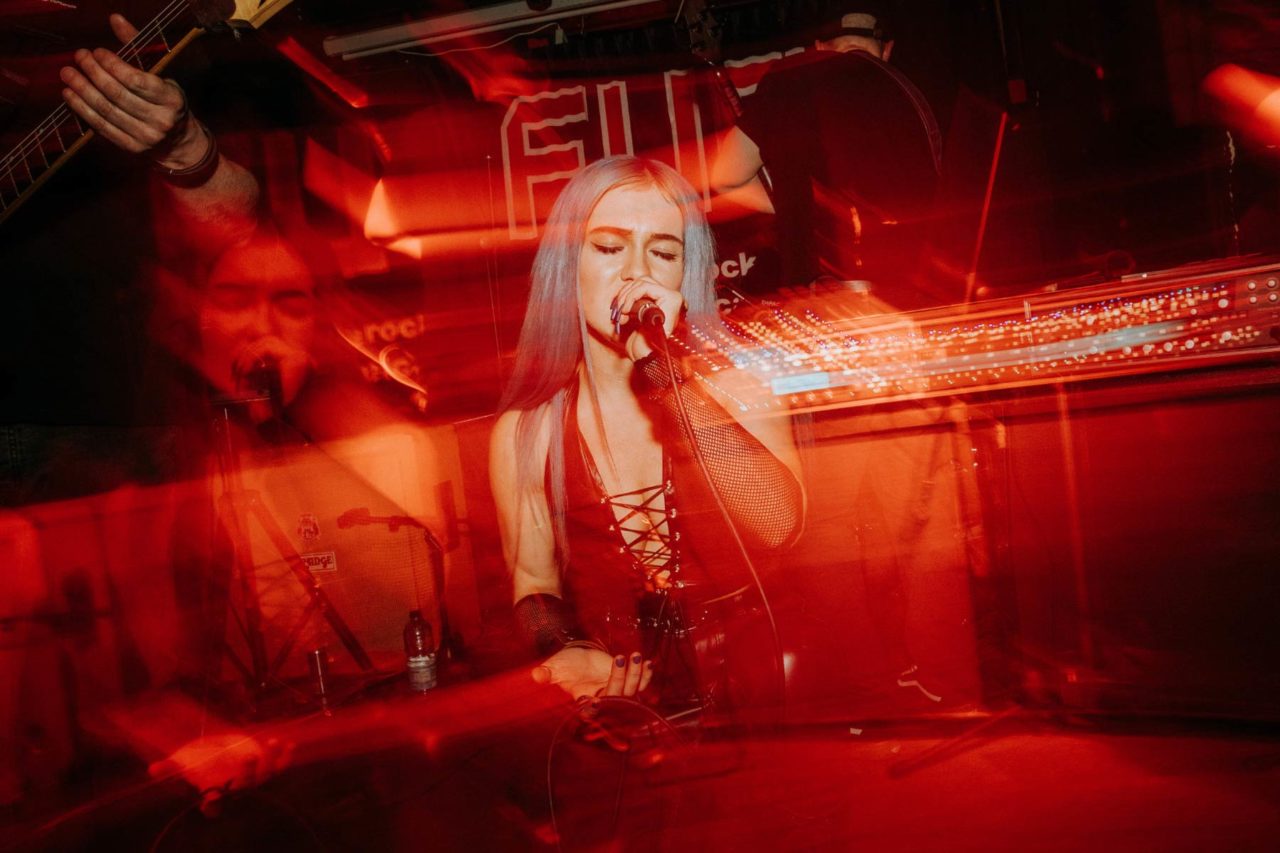 Frontwoman knelt singing into a mic with light and motion blur around her