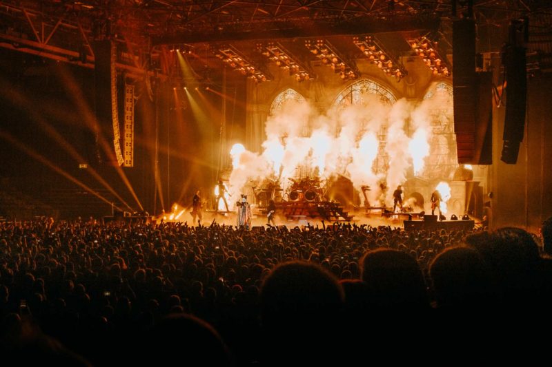 The band Ghost on stage in huge arena with wall of fire exploding behind them
