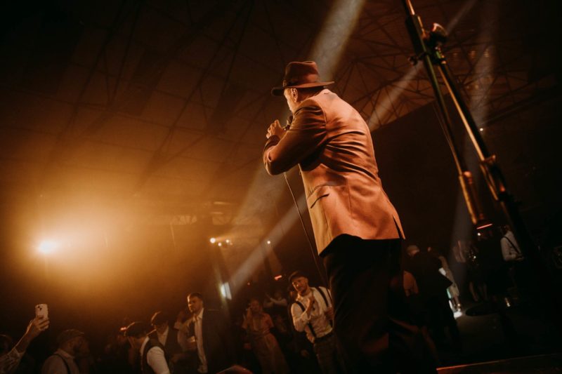 Frontman of swing band stood at front of stage illuminated by spotlight as he sings to the audience