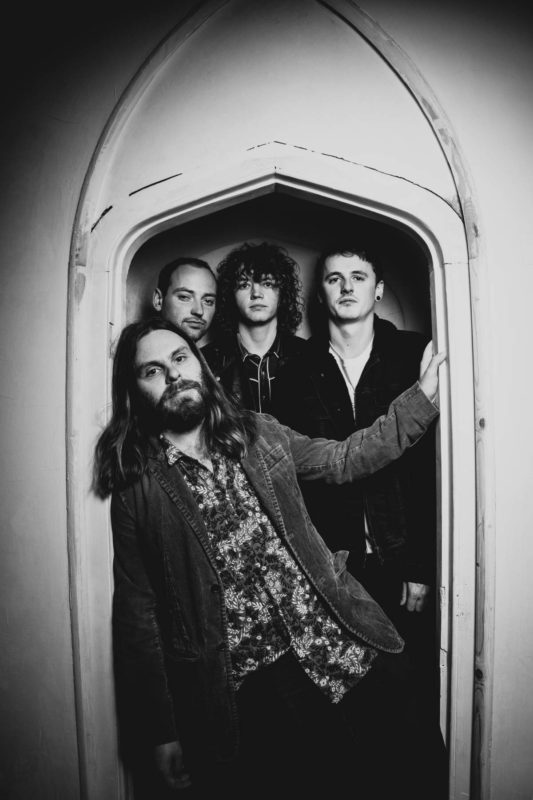 Gritty black and white shot of four men squeezed into a gothic stone arch