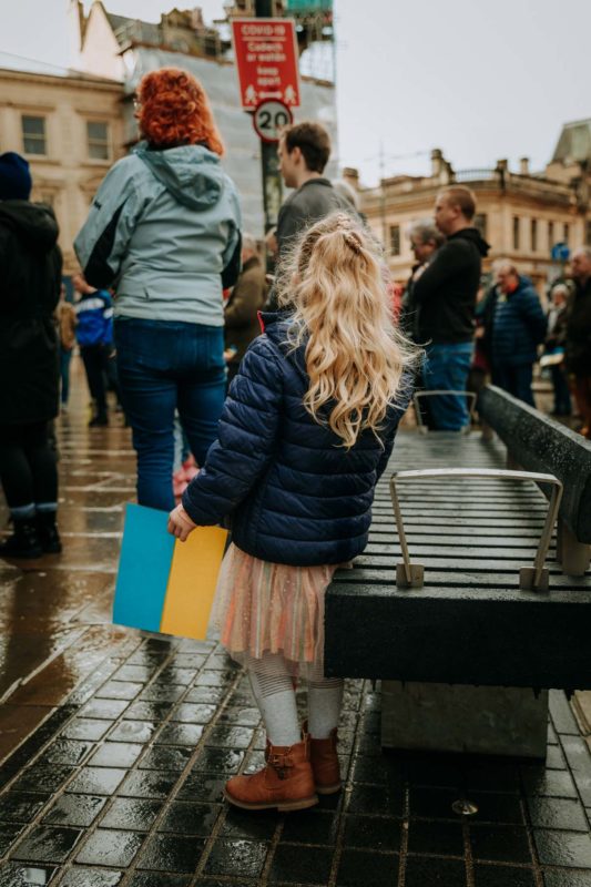 An anonymous image of a young blonde girl with her back to the camera holding a blue and yellow flag