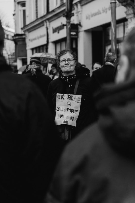 A black and white portrait of a lady holding up a painting of Welsh and Ukrainain flags together with a Welsh message written on it