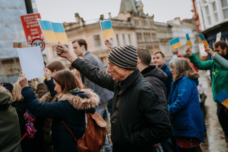 A group of people with a man in the foreground holding up a blue and yellow flag