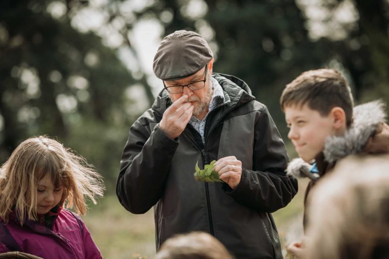 Father stood with you ng daughter holding a plant and smelling his fingers