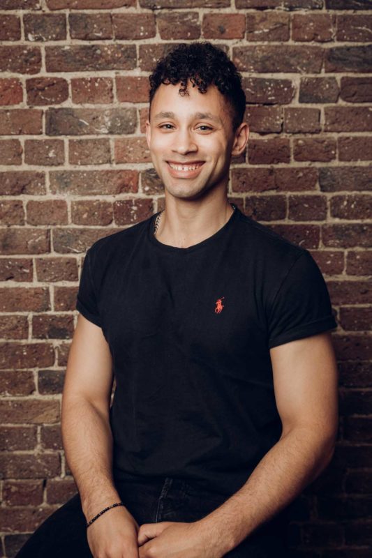 Tall man sat on stool smiling to the camera during a studio shoot