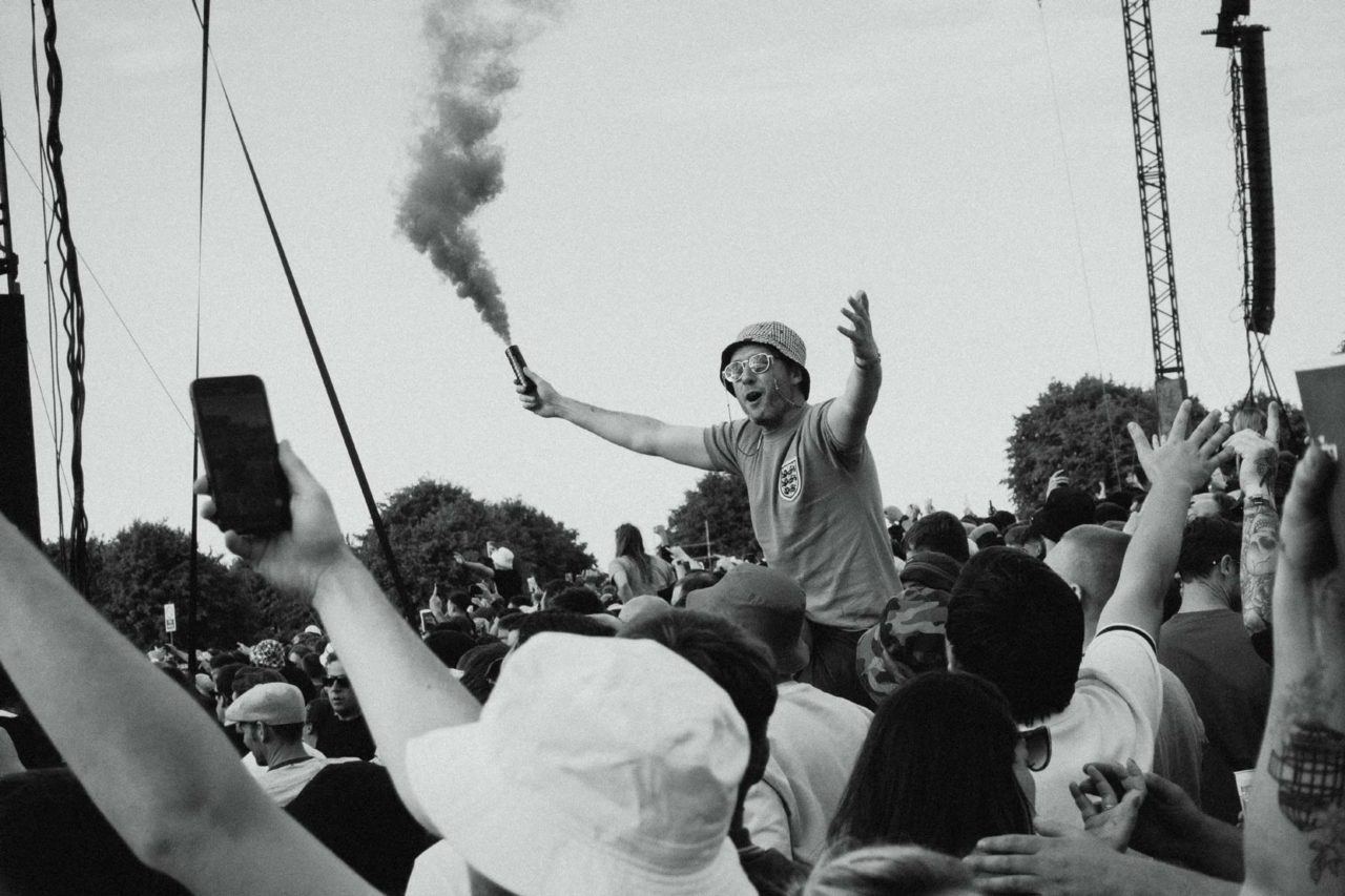 Ecstatic music fan sat on a friend's shoulders waving a smoke grenade in pure enjoyment