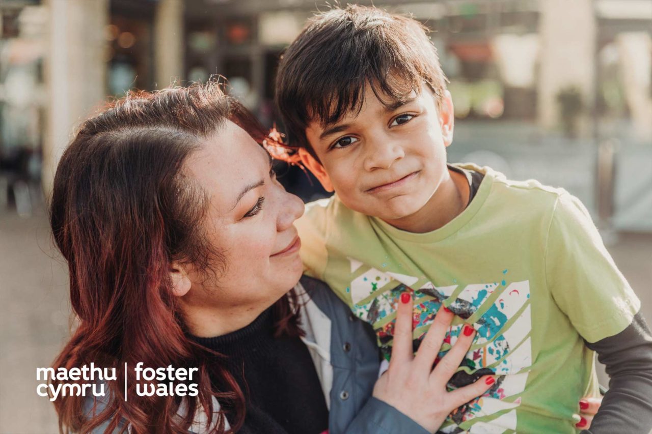 Happy looking child smiling at the camera while his foster mum looks at him lovingly
