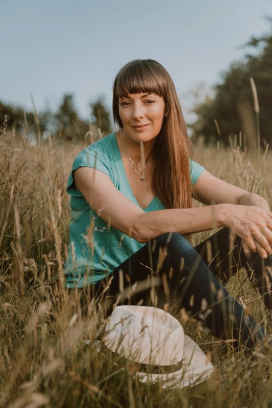 Woman smiling towards camera with a hat in the foreground in the middle of a field