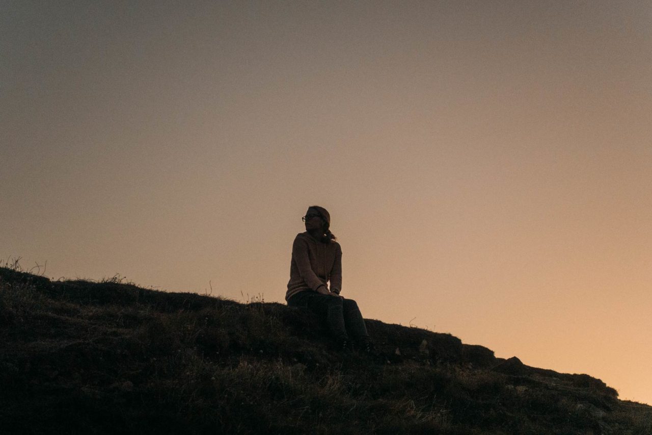 Silhouette of woman sat against the rising sun