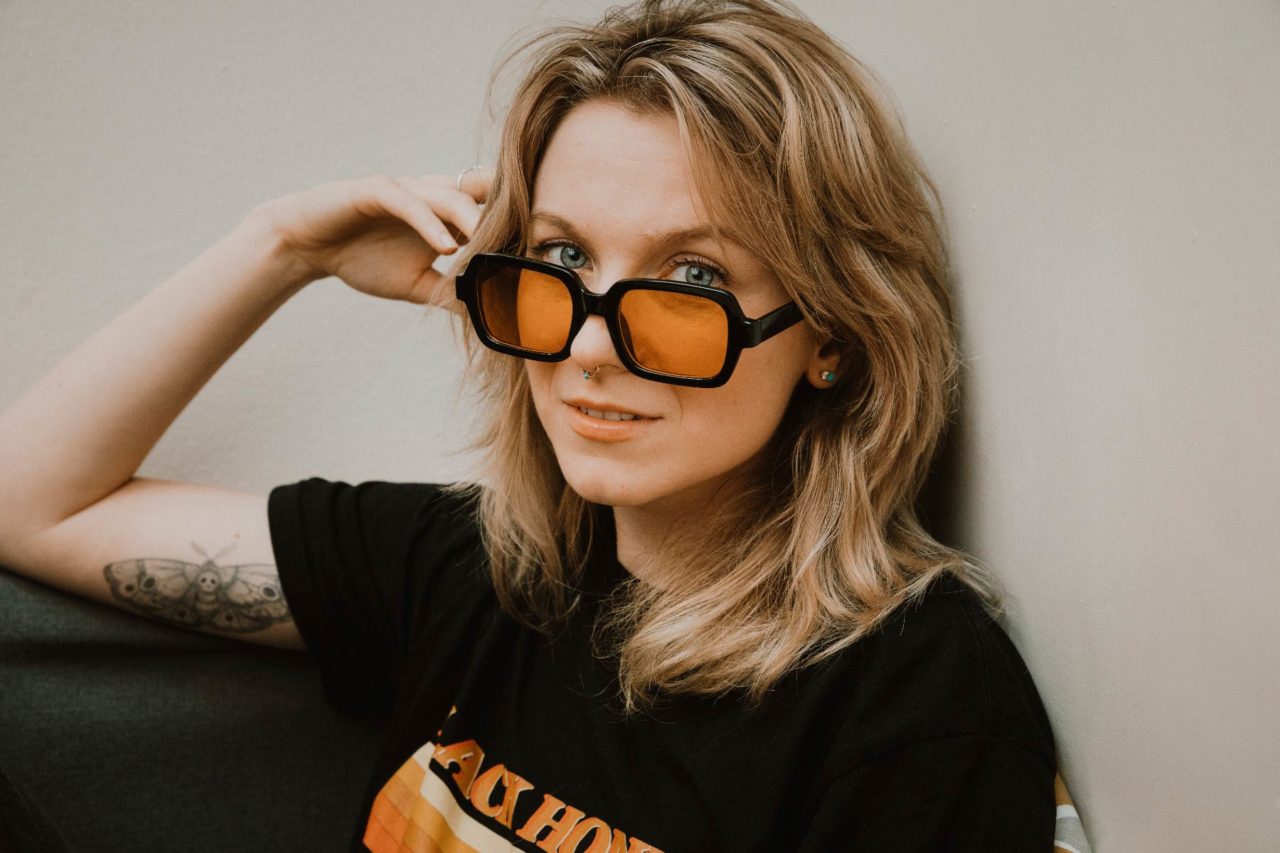Blonde girl staring into the camera looking over the top of 80's retro shades