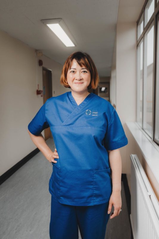 Friendly NHS nursed dress in blue scrubs stood in a hospital corridor resting her hand on her hip