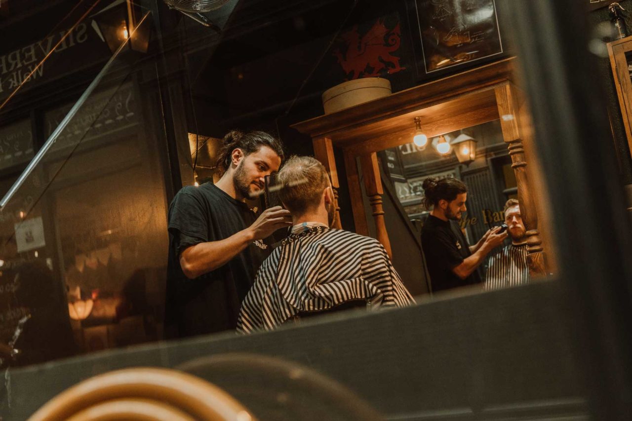 Candid shot of a barber cutting a clients' hair with client's face reflected in a mirror