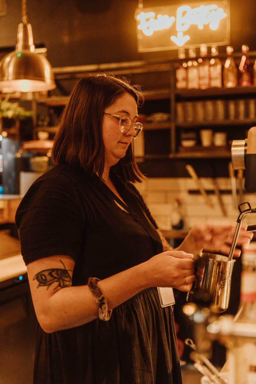 Portrait of a female barista making a coffee, backlit by a warm yellow sign