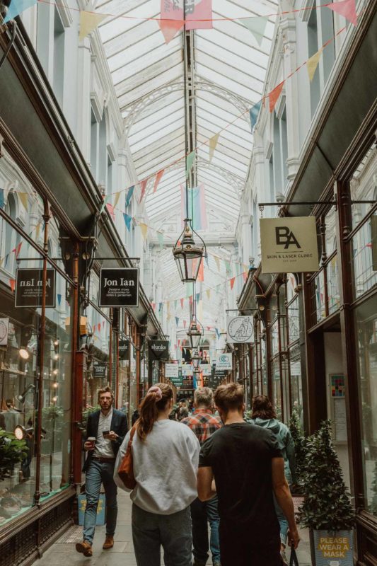 Tall portrait image of a busy Morgan Arcade with colourful flags draped from the roof with people shopping below