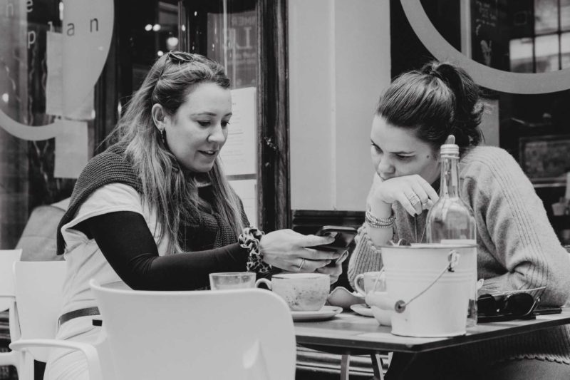 Two female friends sat at a table in Morgan Arcade in black and white