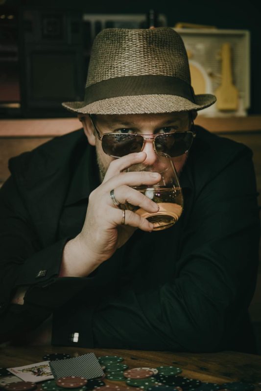 Close up of man peering over sunglasses sipping whiskey