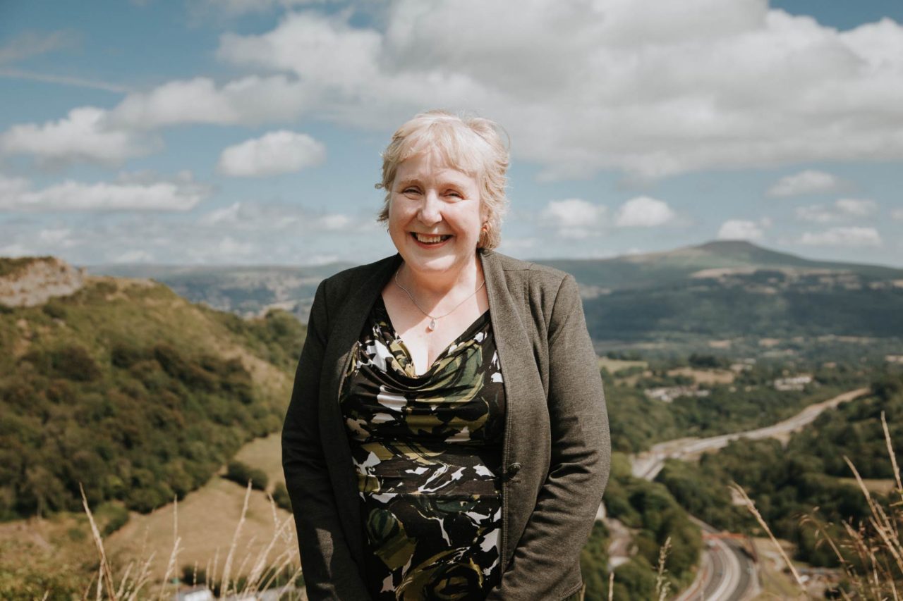 Smiling lady stood atop a hill overlooking rural countryside on a glorious sunny day