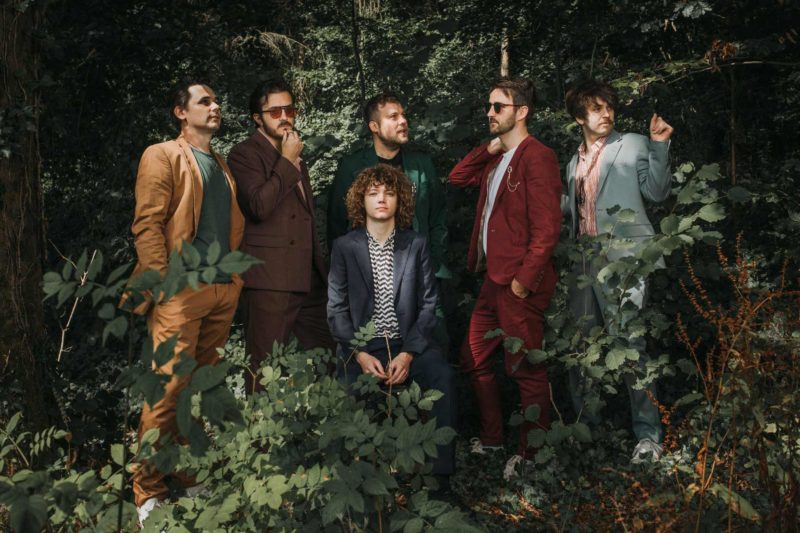 Folk band in colourful suits stood amongst the forest pulling comical poses