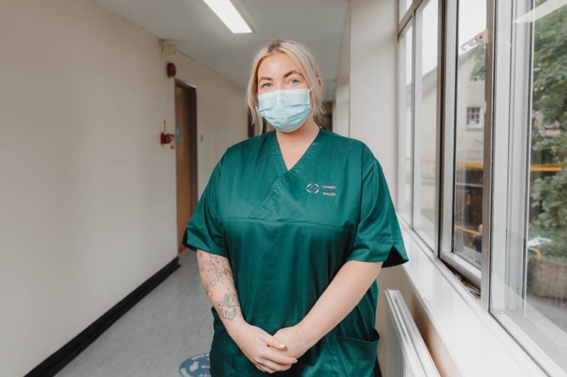 NHS nurse stood in green scrubs smiling in a hospital corridor