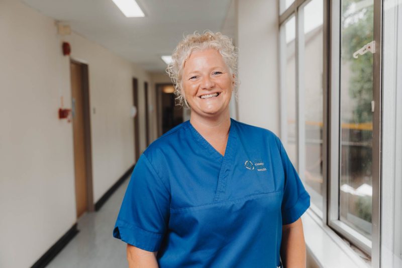 NHS nurse stood in blue scrubs smiling in a hospital corridor