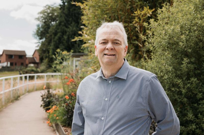 Friendly male councillor stood in front of orange flowers smiling to the camera in the grounds of Mardy Park